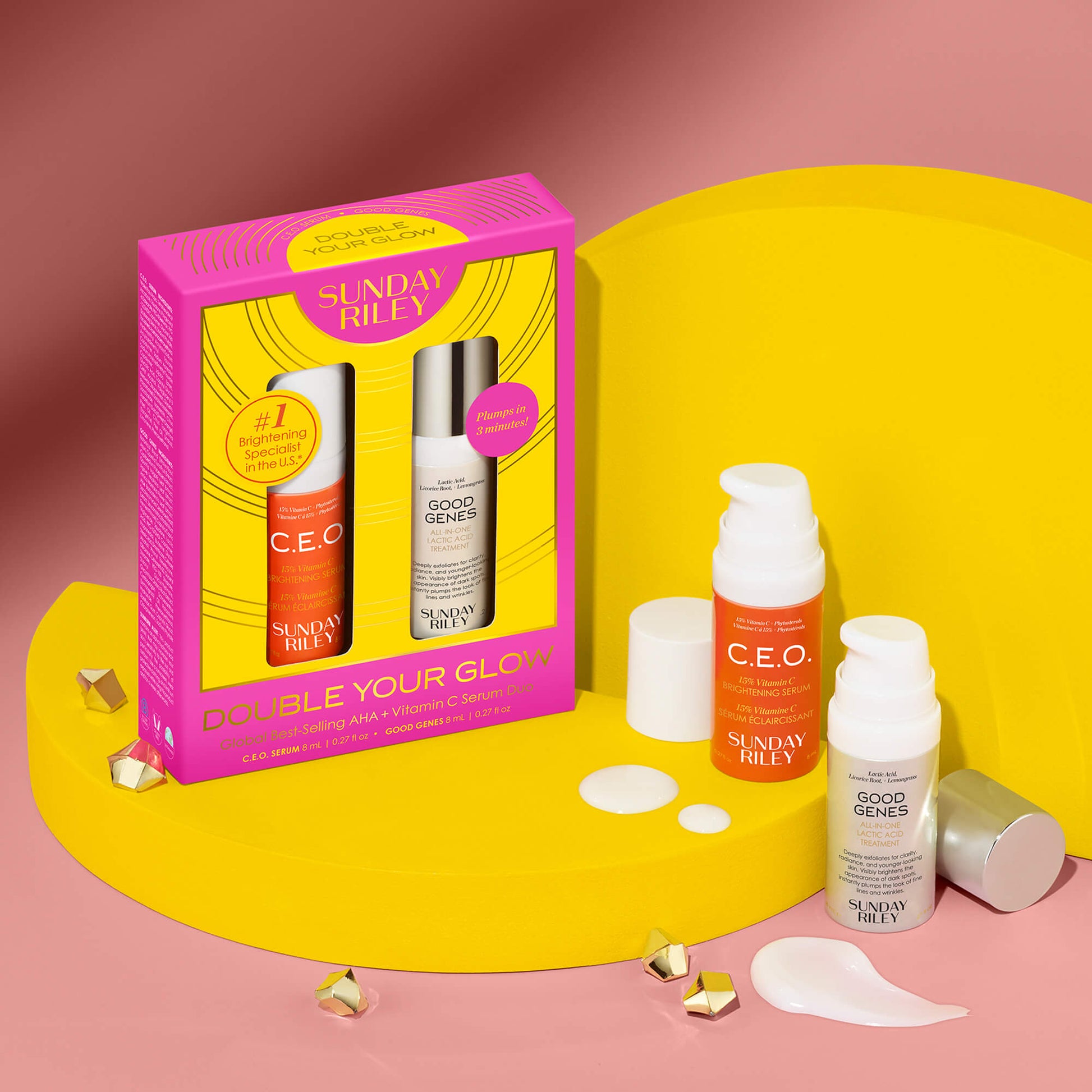Double Your Glow - Global Best Selling AHA + Vitamin C Serum Duo pack shot with the product bottles in front of pack shot with product bottles on the side and both on top of a yellow prop stand