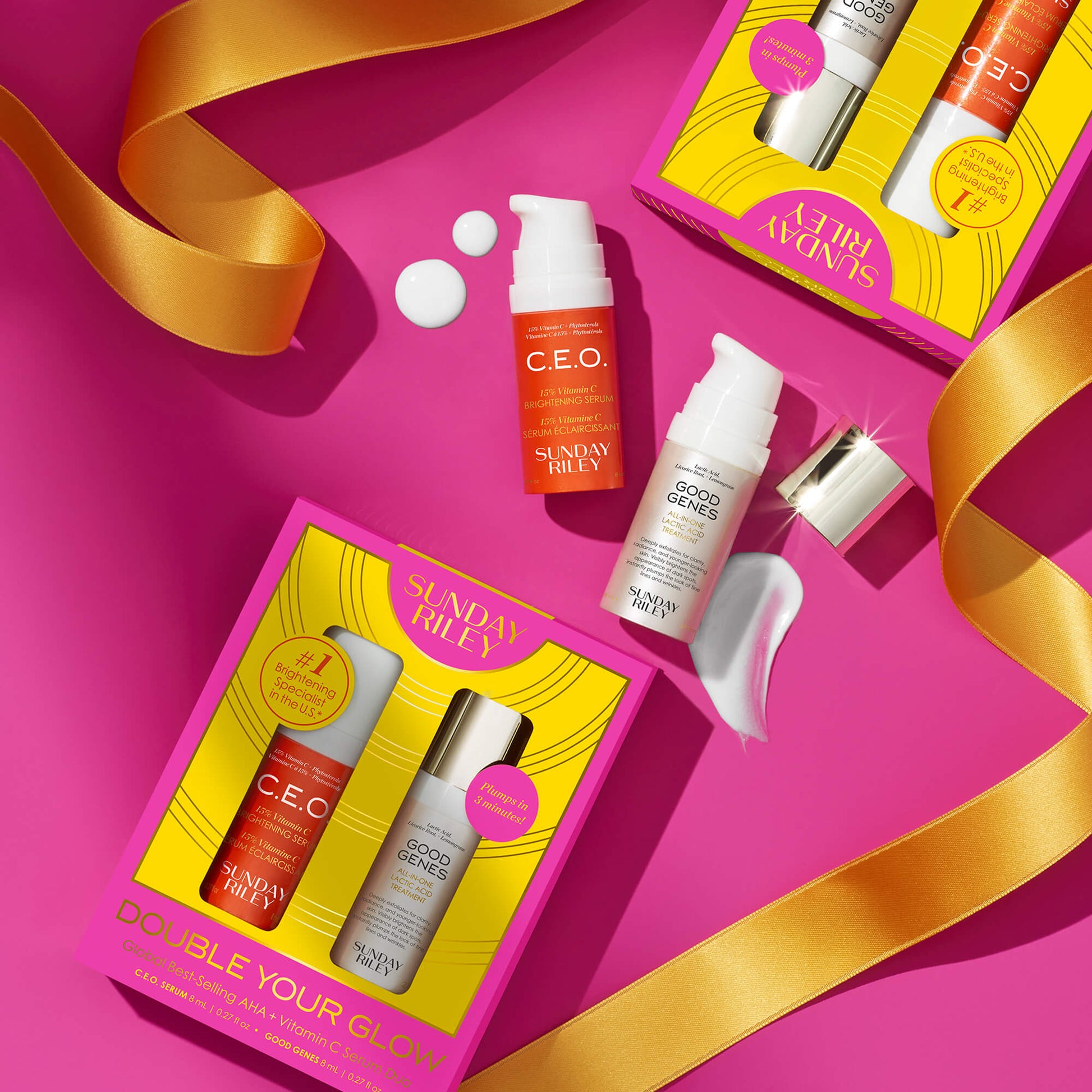 Double Your Glow - Global Best Selling AHA + Vitamin C Serum Duo pack shot with the product bottles in front of pack shot laying down with product bottles laying down above it, on top of a pink background and yellow ribbons